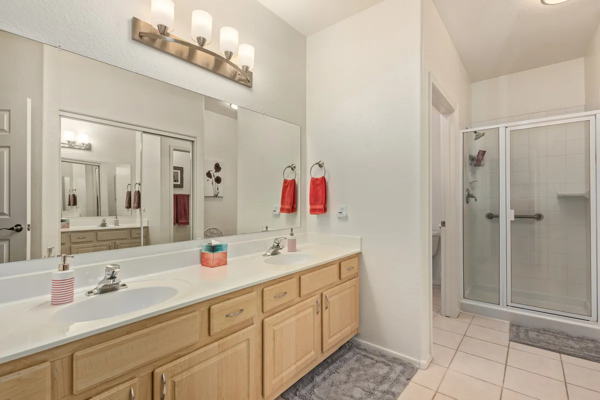 A modern bathroom with a spacious double sink vanity, large mirror, and a glass-enclosed shower. The surfaces are clean and inviting, lending a spa-like feeling to the space and ensuring ample room for personal routines.