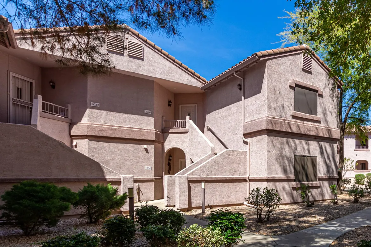 This exterior shot showcases the architectural features of the building, beautifully landscaped shrubs and bushes, and a prominent staircase leading to the entrance. The scene is bright and inviting, epitomizing the welcoming atmosphere of the neighborhood.