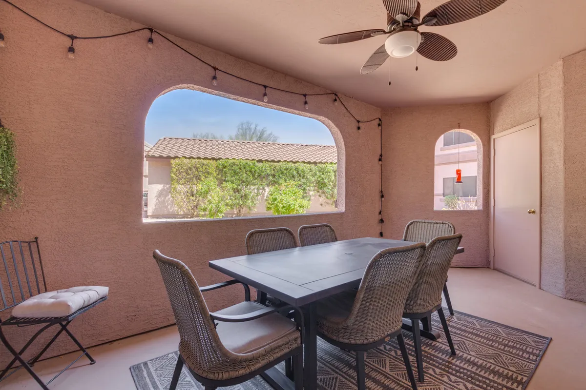 An interior dining area framed by a large window with views outside. The scene is bright, casual, and welcoming, with a ceiling fan above and the promise of sunset views or morning light streaming in.