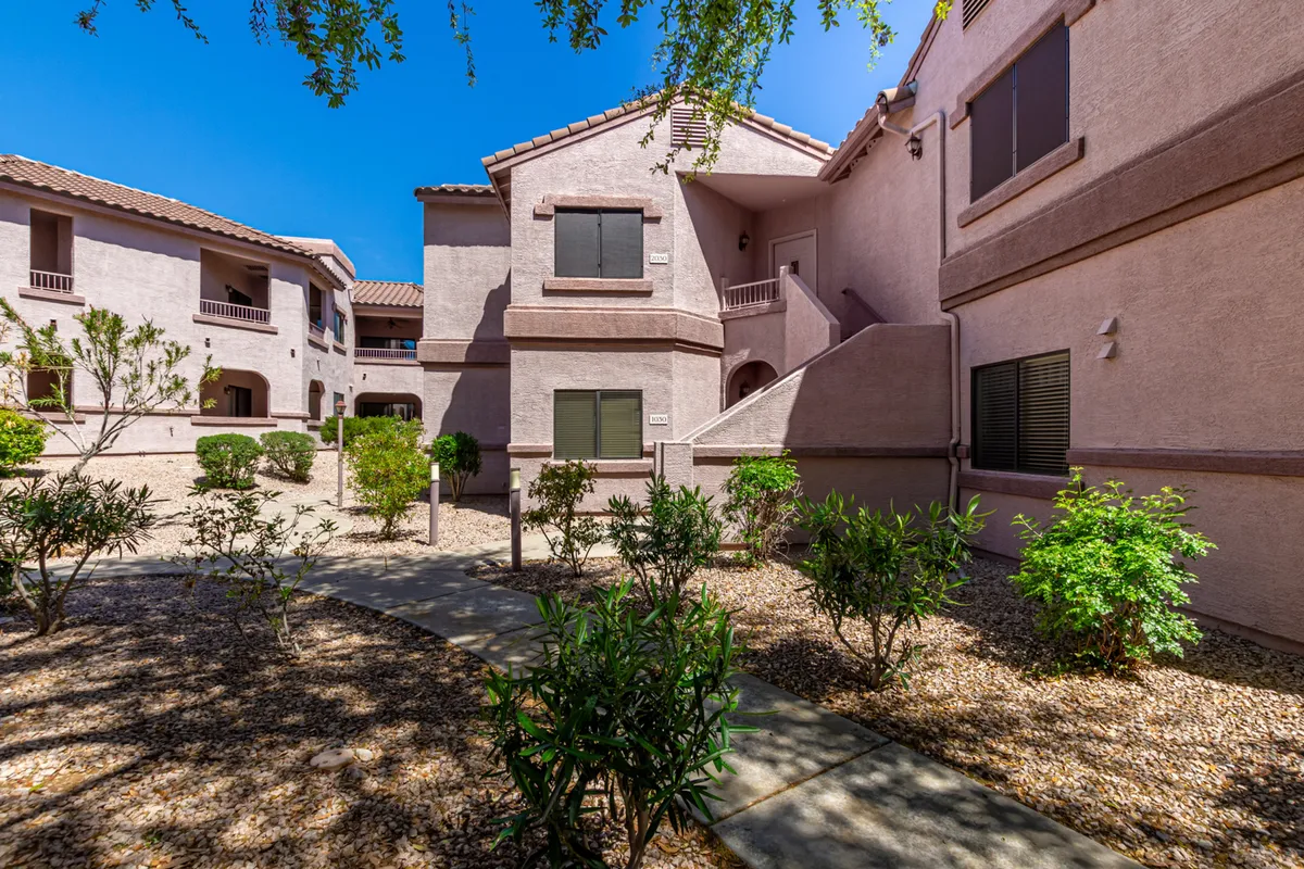 The photo captures the building's attractive facade, a meandering pathway, and well-maintained landscaped areas. Residents can be seen strolling or socializing in the peaceful courtyard, highlighting the communal atmosphere of the grounds.