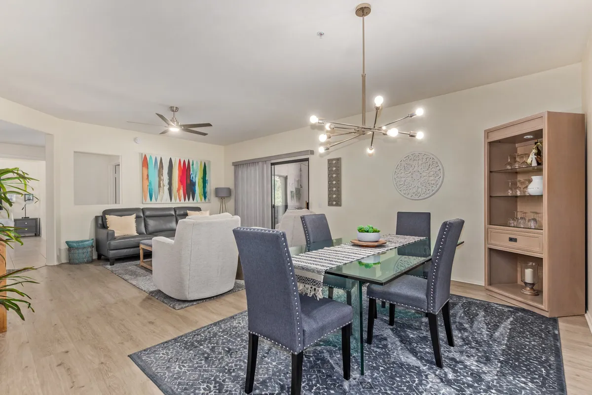 A view combining a modern dining table with comfortable chairs and a cozy living area, featuring colorful wall art and a contemporary chandelier. The layout highlights the seamless flow between living and dining spaces, ideal for unwinding or entertaining guests.