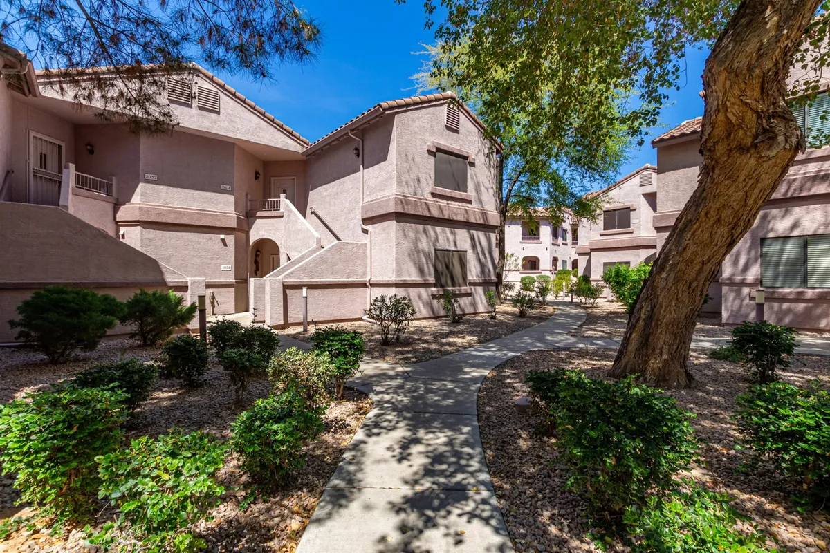 This exterior image features a welcoming pathway lined with lush greenery and leads to the apartment buildings within the gated community. The scene evokes a sense of tranquility and community, ideal for long strolls or casual gatherings outdoors.