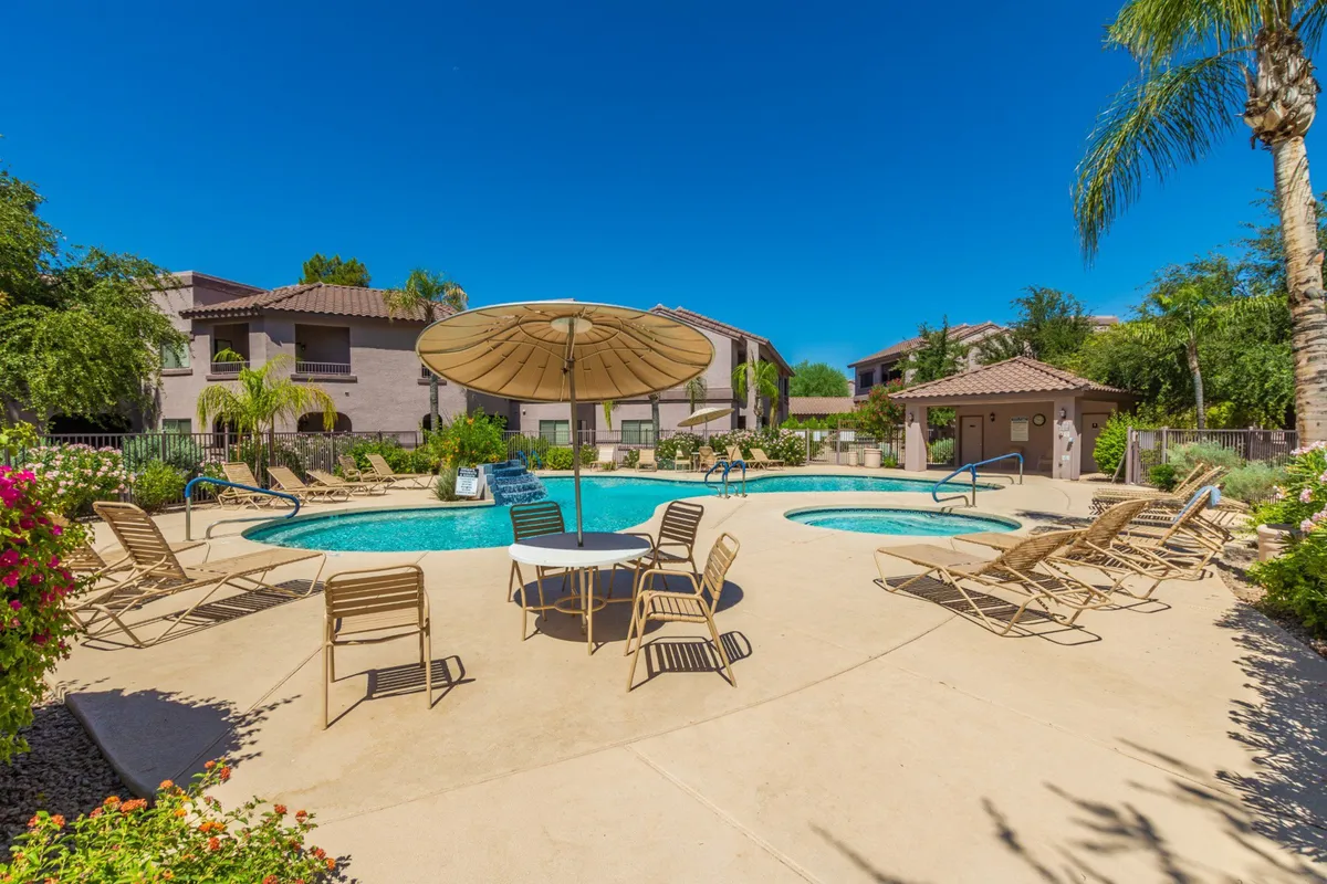 This exterior image features a sparkling swimming pool surrounded by lounge chairs, umbrellas, and lush greenery. The scene exudes a leisurely, family-friendly vibe, with ample space for sunbathing, swimming, and socializing. The sunset lighting adds to the inviting, relaxing mood.