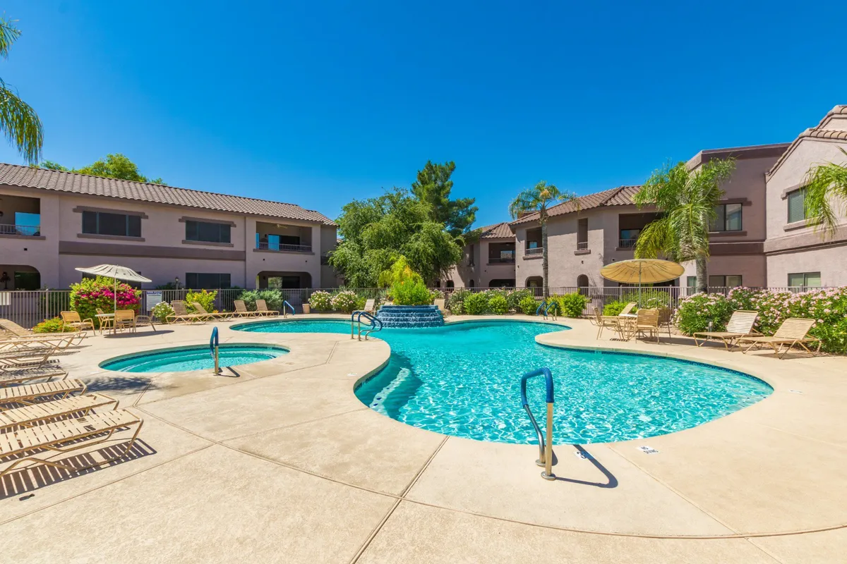This image offers a sweeping view of the community's heated swimming pool surrounded by inviting lounge chairs, lush landscaped greenery, and a charming fountain feature. The tranquil pool scene exudes relaxation, with sunset lighting creating a resort-like atmosphere.