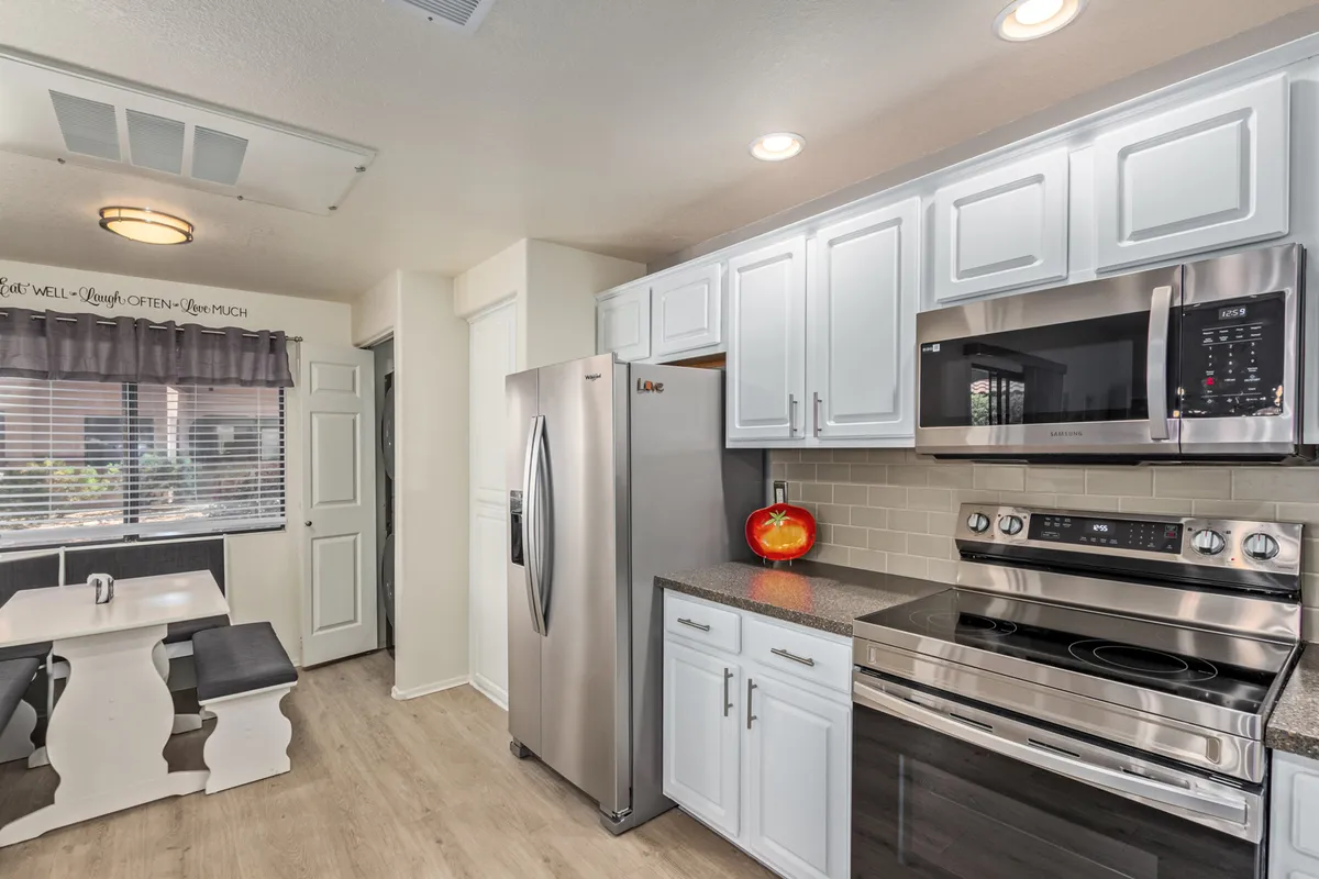 A bright and cheerful dining space with a modern table, comfortable seating, stainless steel appliances, and decorative touches like a fruit centerpiece. Natural light fills the room, contributing to an uplifting and secure feeling.