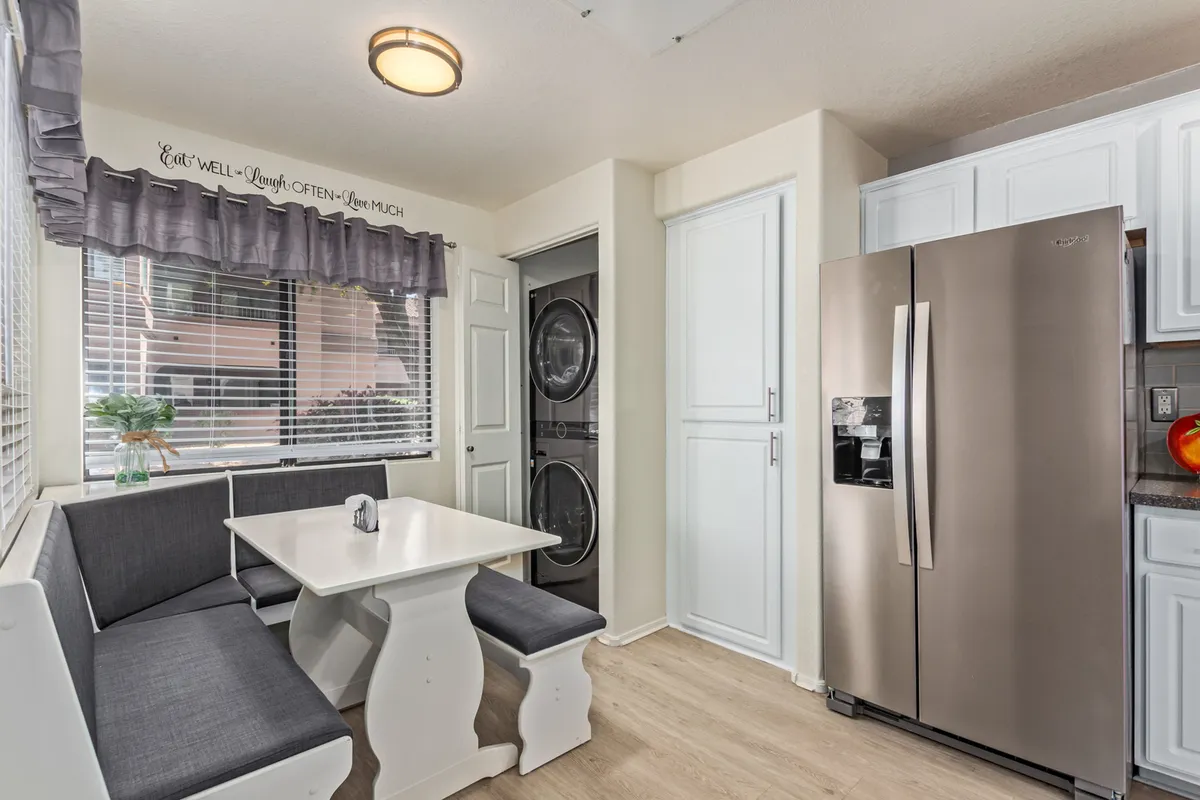 A cozy breakfast nook situated adjacent to a modern refrigerator, accented by decorative wall text. The nook is designed for casual meals and intimate gatherings, with natural light creating a warm, inviting atmosphere.
